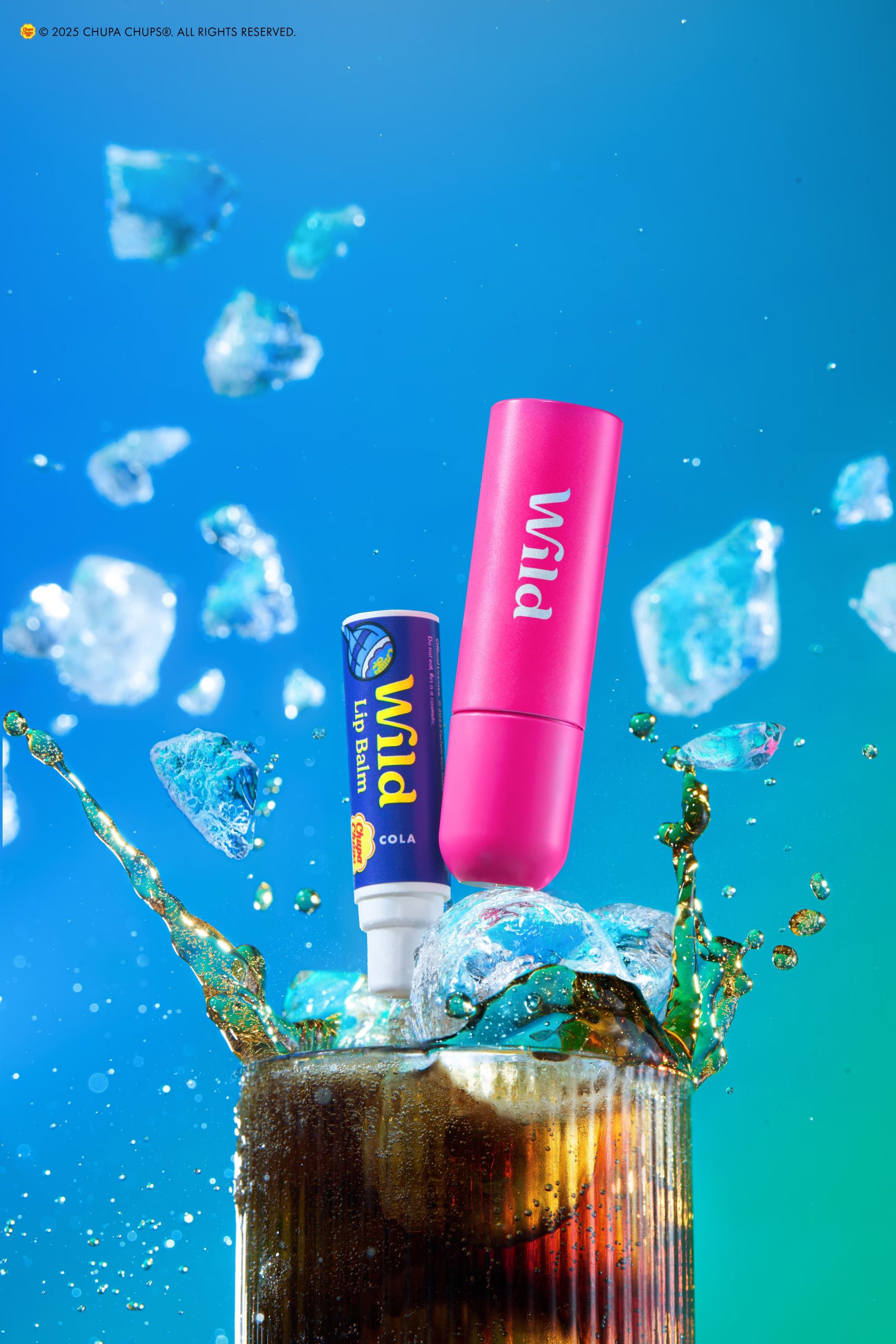 Two lip care products displayed above a glass of cola with ice, surrounded by dynamic splashes and floating ice cubes against a bright blue background.